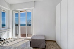 A room with a view to the sea, a sliding glass door, a small table, and a chair.