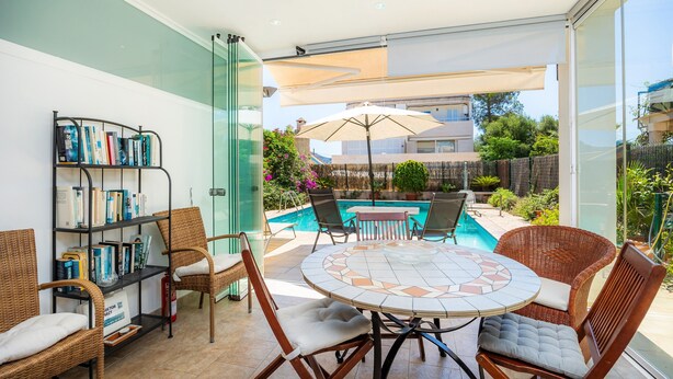 Eine sonnige Terrasse mit Pool, Korbmöbeln und einer Bücherwand.