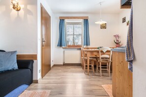 Kompakti oleskelutila, jossa on sohva, ruokapöytä tuoleineen, ikkuna verhoilla ja patteri.
