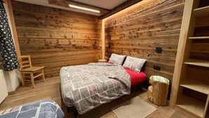 Una camera da letto con una parete in legno, un letto con copriletto decorato, una sedia e un piccolo sgabello di legno.