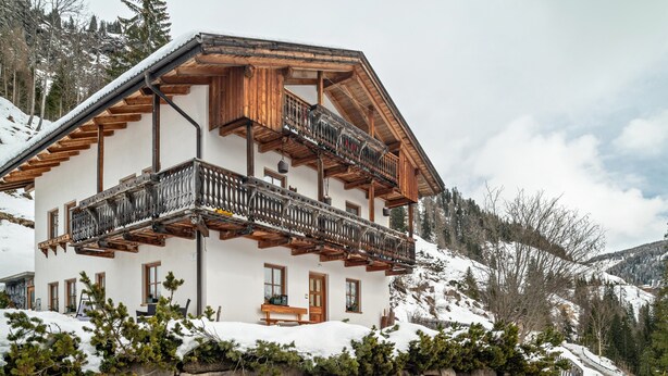 Una chalet a più piani con balconi, pareti in pietra e un paesaggio montuoso innevato.