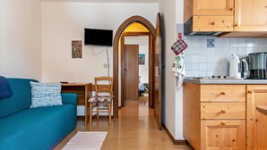 Un espacio habitable compacto con sofá, una silla, zona de cocina con armarios y estufa, y televisión montada en la pared.