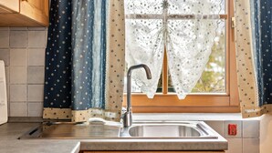 Una cocina con un lavabo, una ventana con cortinas de encaje y armarios de madera.