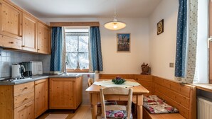 Una cocina con armarios de madera, una mesa de comedor, un banco y una ventana con cortinas.