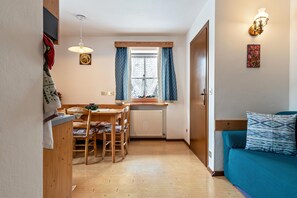 Kompakti huone, jossa on ruokailutila, ikkuna verhoilla, kuviollinen vuodevaatteilla varustettu sänky ja seinälle asennettu valaisin.