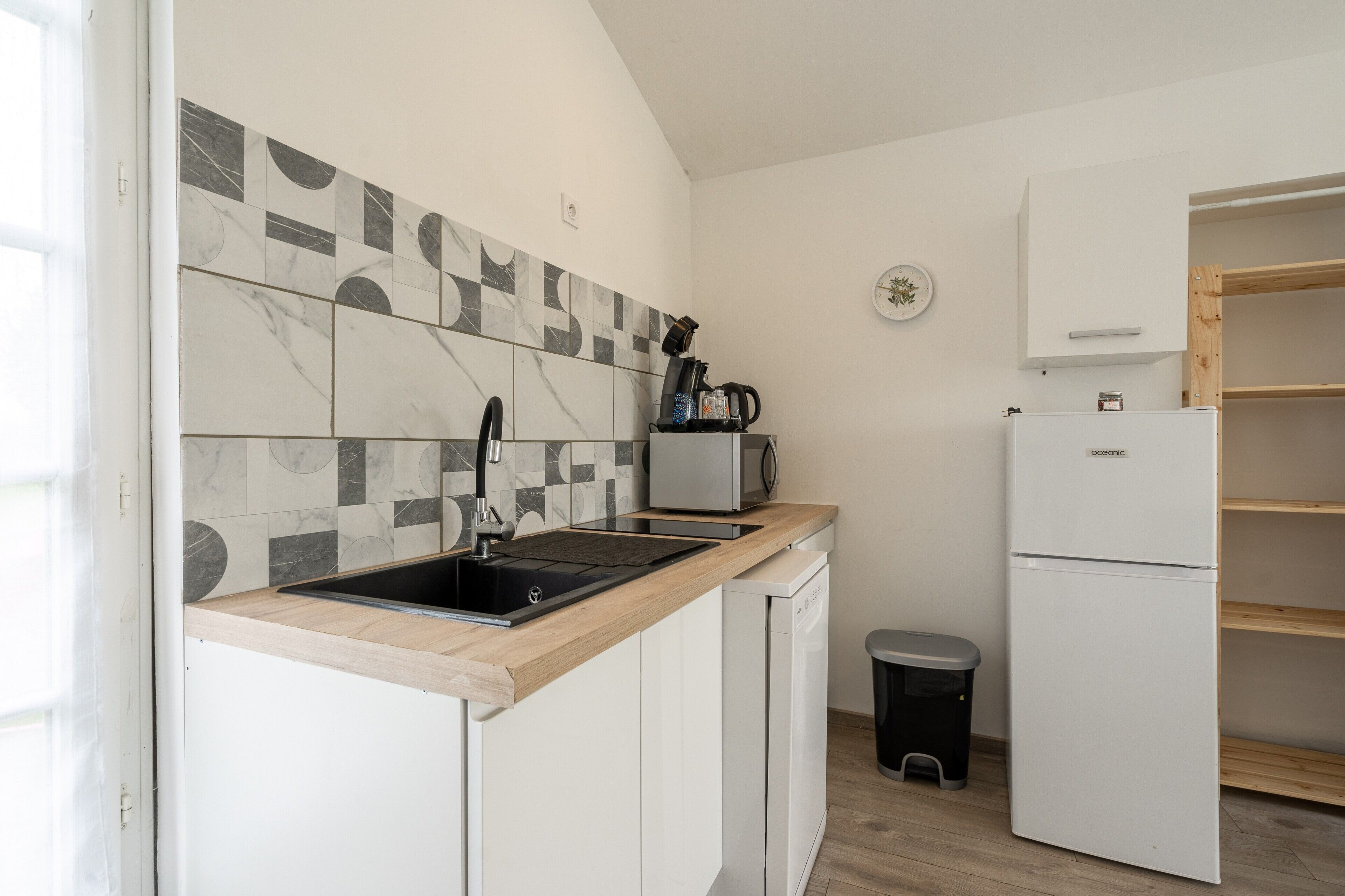 Una cocina compacta con lavamanos, cafetera y refrigerador.