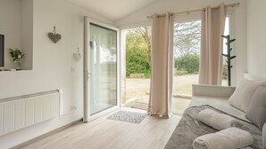 Una habitación con cama, televisor, radiador, puerta de cristal corredera y vistas a la vegetación exterior.