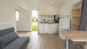 Cocina funcional con armarios blancos, un microondas y un refrigerador. En la sala de estar, hay un sofá gris y una mesa de madera.