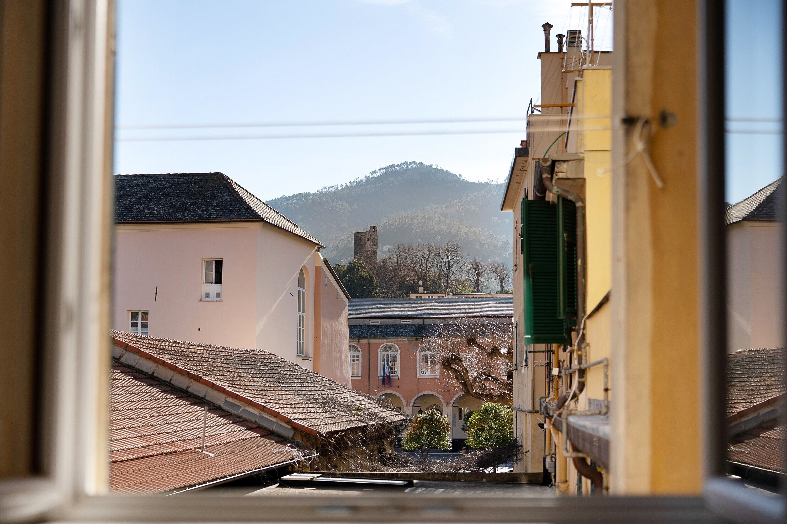 Una veduta attraverso una finestra mostra un edificio con tetto in tegole, un edificio rosa e una collina sullo sfondo.