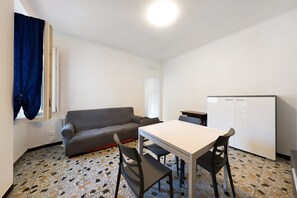 A compact living space with a sofa, a dining table, chairs, a refrigerator, and a patterned floor.