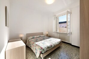 A bedroom with a bed, bedside lamps, a window with an open shutter, and a radiator.