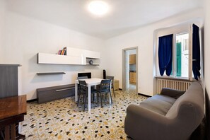 A modern living room with a sofa, a dining table with chairs, a white cabinet, and a patterned floor.