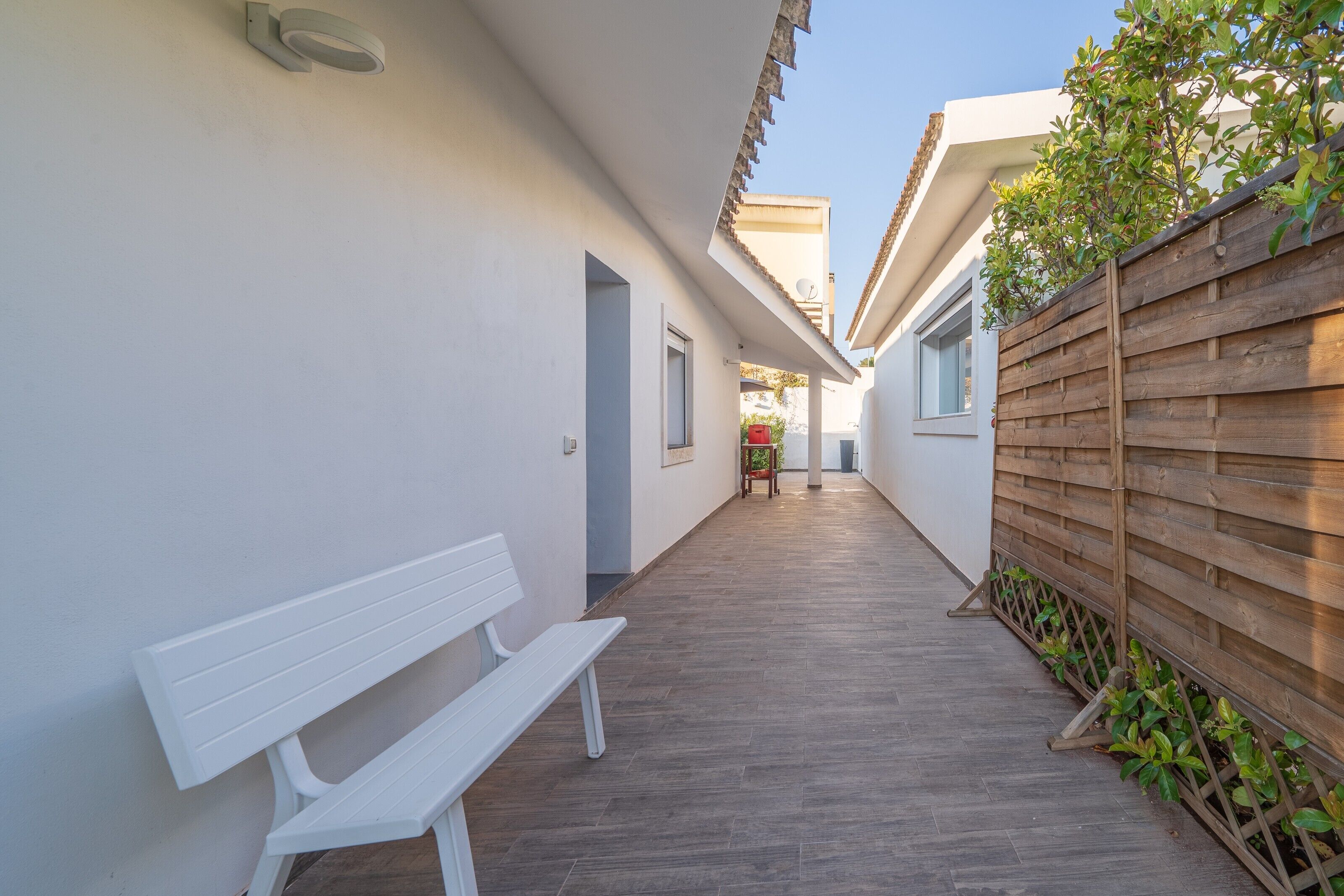 A narrow corridor with a white bench, wooden fence, and a door at the end.