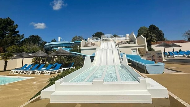Een waterpark met een grote glijbaan, ligbedden en een helderblauwe lucht.