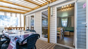 Een terras buiten met een eettafel, een houten terras en een schuifpui die naar een binnenruimte leidt.