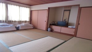 Una habitación tradicional japonesa con suelo de tatami, una cama con almohadas, un televisor y un armario.
