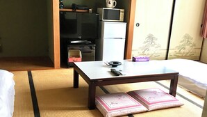 Una stanza con pavimento in tatami, un letto, un tavolino con un telecomando, un forno a microonde e un frigorifero.