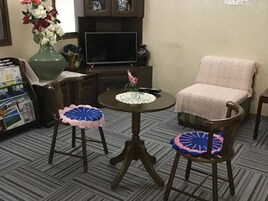 Una sala de estar con televisor, una mesa de centro, dos sillas con protectores de asiento de ganchillo, un florero con flores y una estantería con revistas.