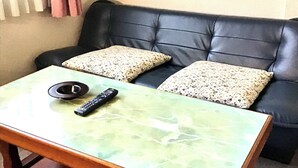Un soggiorno con un tavolino da caffè in marmo verde, due cuscini decorati, un divano in pelle nera e un telecomando sul tavolo.