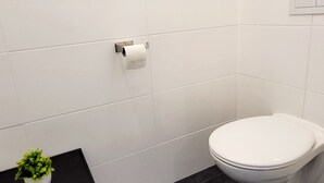 A modern bathroom with white tiles, a toilet, a black sink, and a small potted plant. - Siccardsburggasse Apartment With 1 Balcony (Vienna)