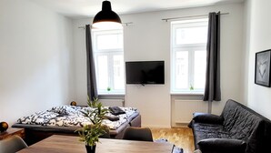 A modern living room with a wooden dining table, a sofa, and a TV mounted on the wall. - Siccardsburggasse Apartment With 1 Balcony (Vienna)