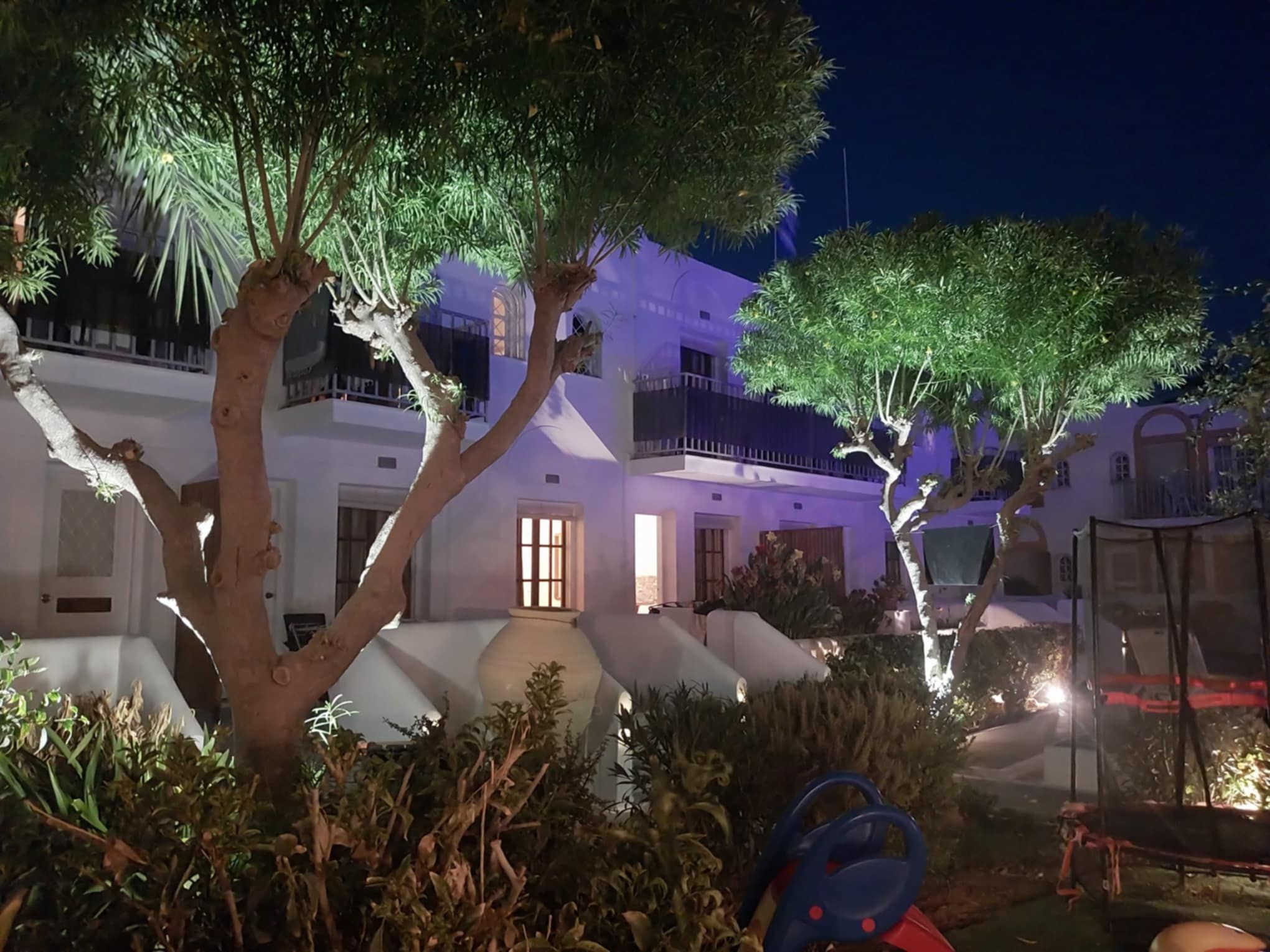 Een gebouw met twee verdiepingen, balkons en een tuin in de nacht.