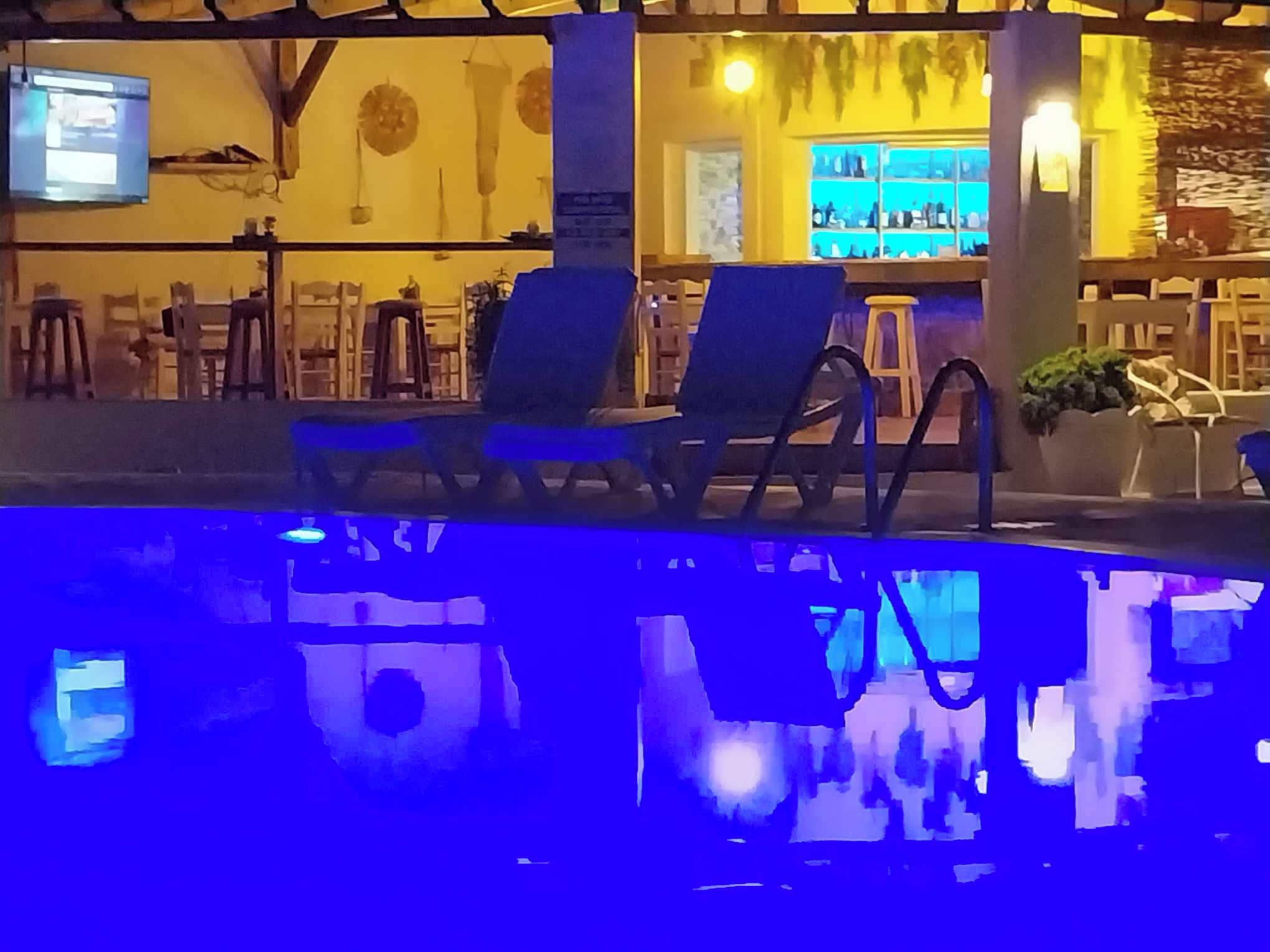 A pool area with lounge chairs and a bar area with a television screen.