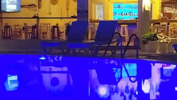 A pool area with lounge chairs and a bar area with a television screen.