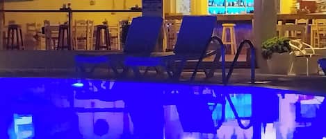 Zona de piscina con sillones de descanso y bar con pantalla de televisión.