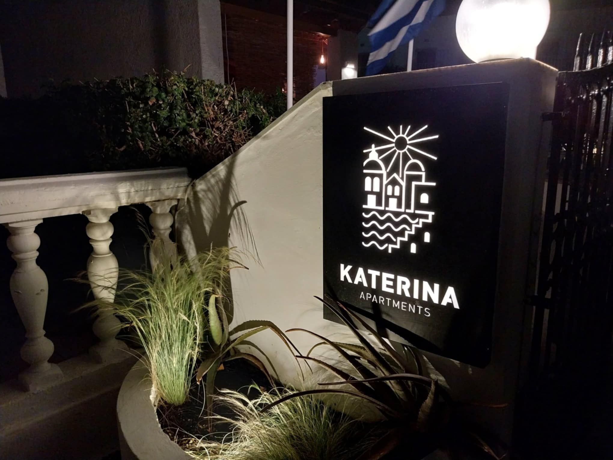 Letrero de Katerina Apartments con un logotipo de un edificio y olas, que indica una ubicación costera.