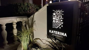 Letrero de Katerina Apartments con un logotipo de un edificio y olas, que indica una ubicación costera.