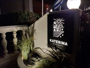 Letrero de Katerina Apartments con un logotipo de un edificio y olas, que indica una ubicación costera.
