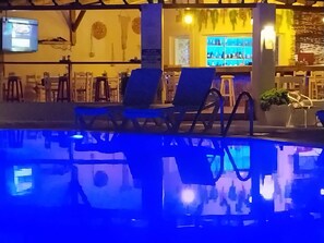 A pool area with lounge chairs and a bar with a blue-lit interior. - Katerina Aprtments (Kalymnos)