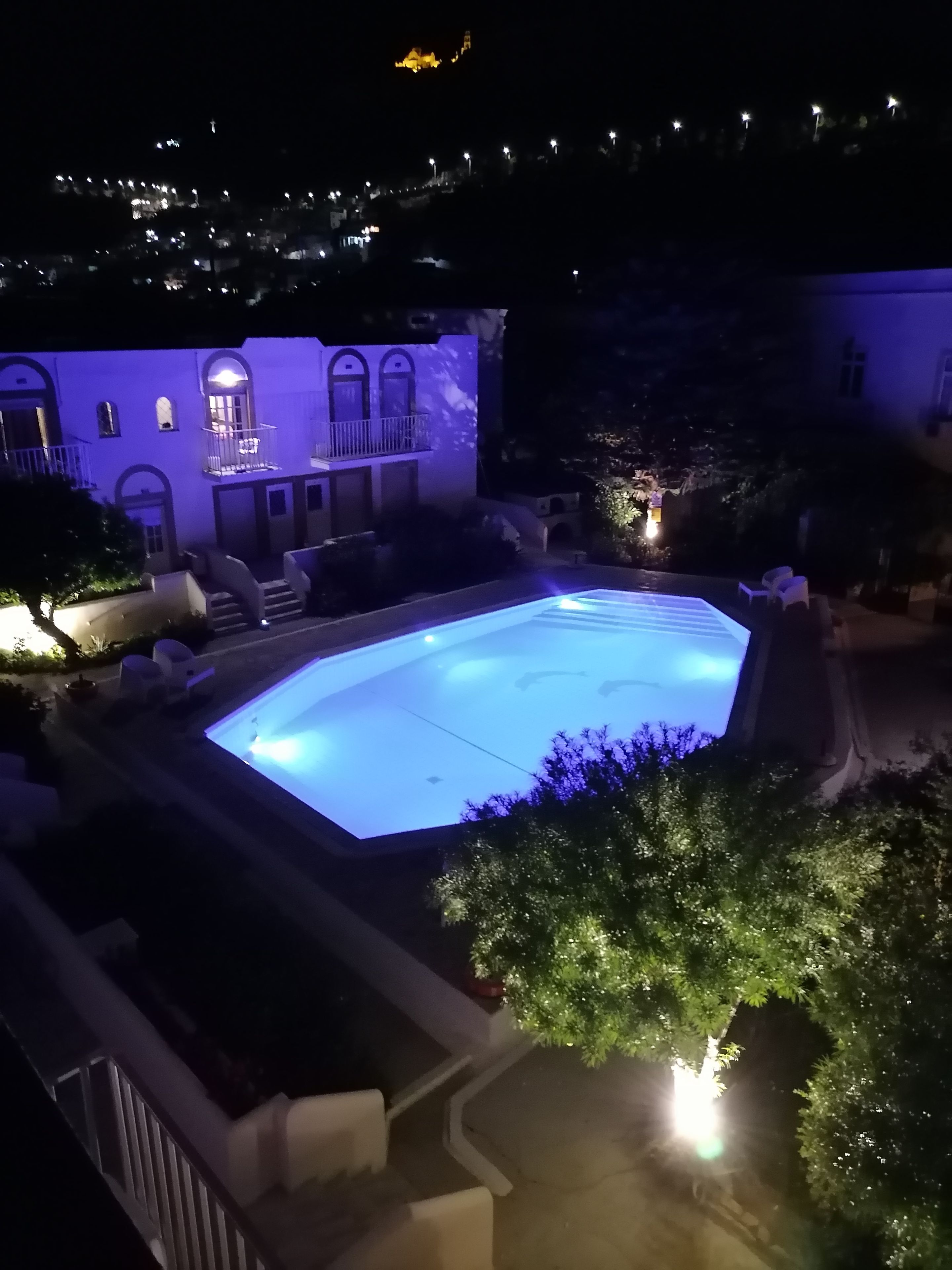 A swimming pool with a geometric shape, surrounded by a building with arched windows and a balcony.