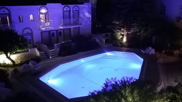 A swimming pool with a geometric shape, surrounded by a building with arched windows and a balcony.