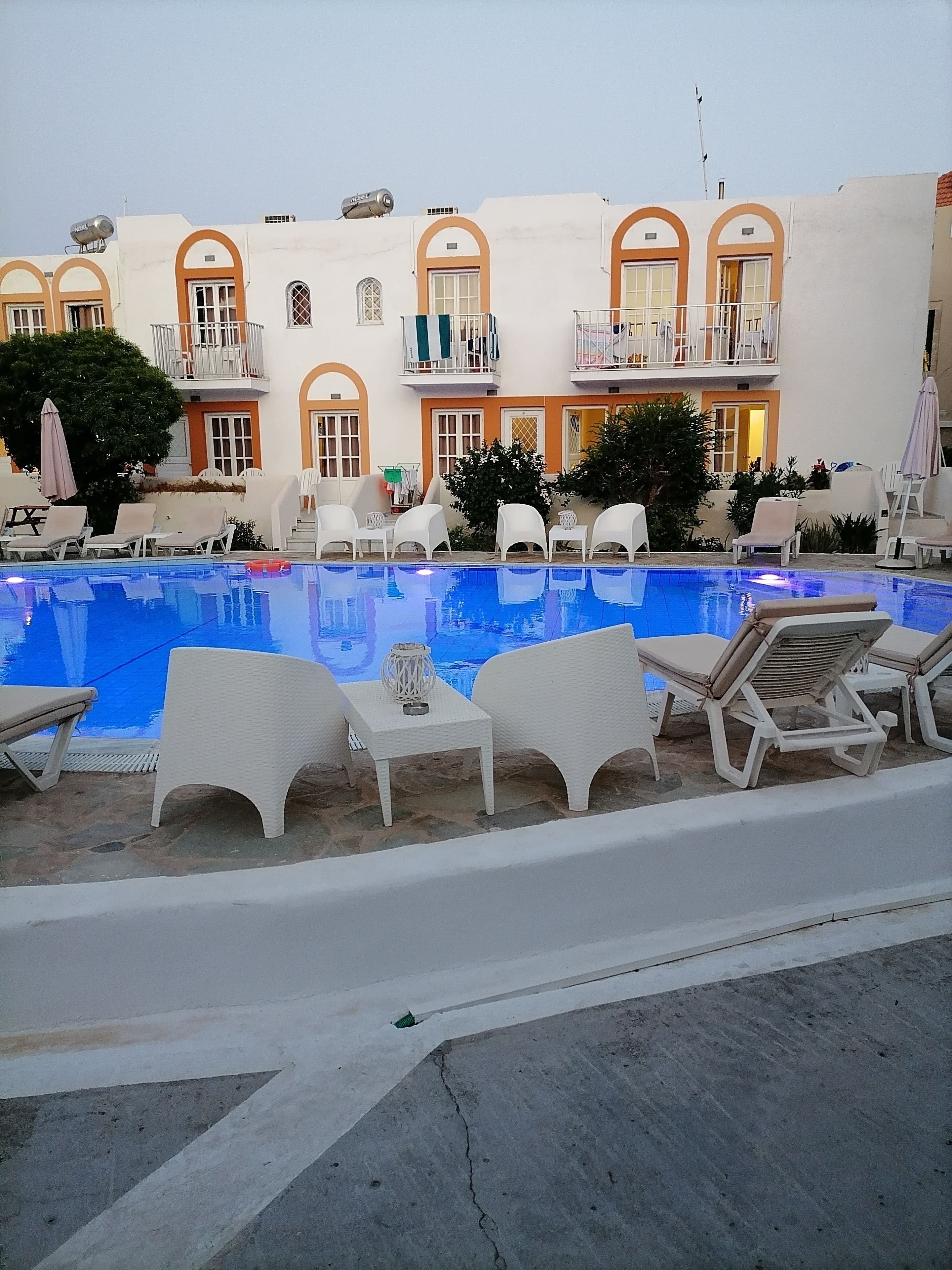 A swimming pool with lounge chairs and a building with arched windows and balconies.