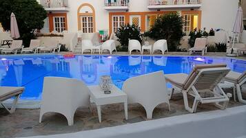 A swimming pool with lounge chairs and a building with arched windows and balconies.
