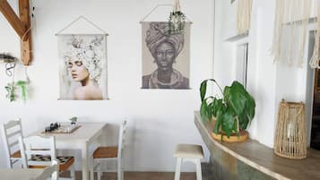 Un comedor con un tablero de ajedrez, sillas blancas, una mesa blanca y dos obras de arte colgando en la pared.
