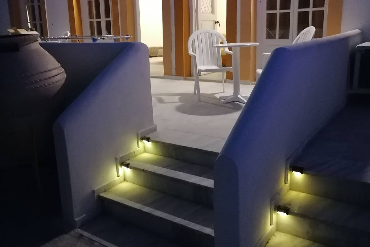Ein überdachter Außenbereich mit Stufen zu einer Tür, einem Grill und einem Tisch mit Stühlen.
