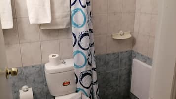 A bathroom with a toilet, a shower curtain, a towel rack, and a toilet paper holder.