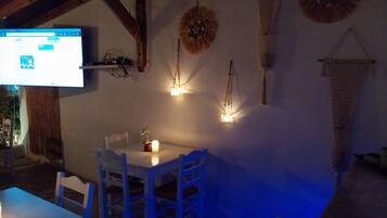 Un coin repas avec une table et des chaises blanches, une bougie et des lampes fixées au mur.