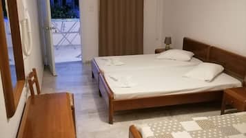 A bedroom with a bed, a desk, and a chair. There is a window with curtains, an air conditioning unit, and a view of the outside.