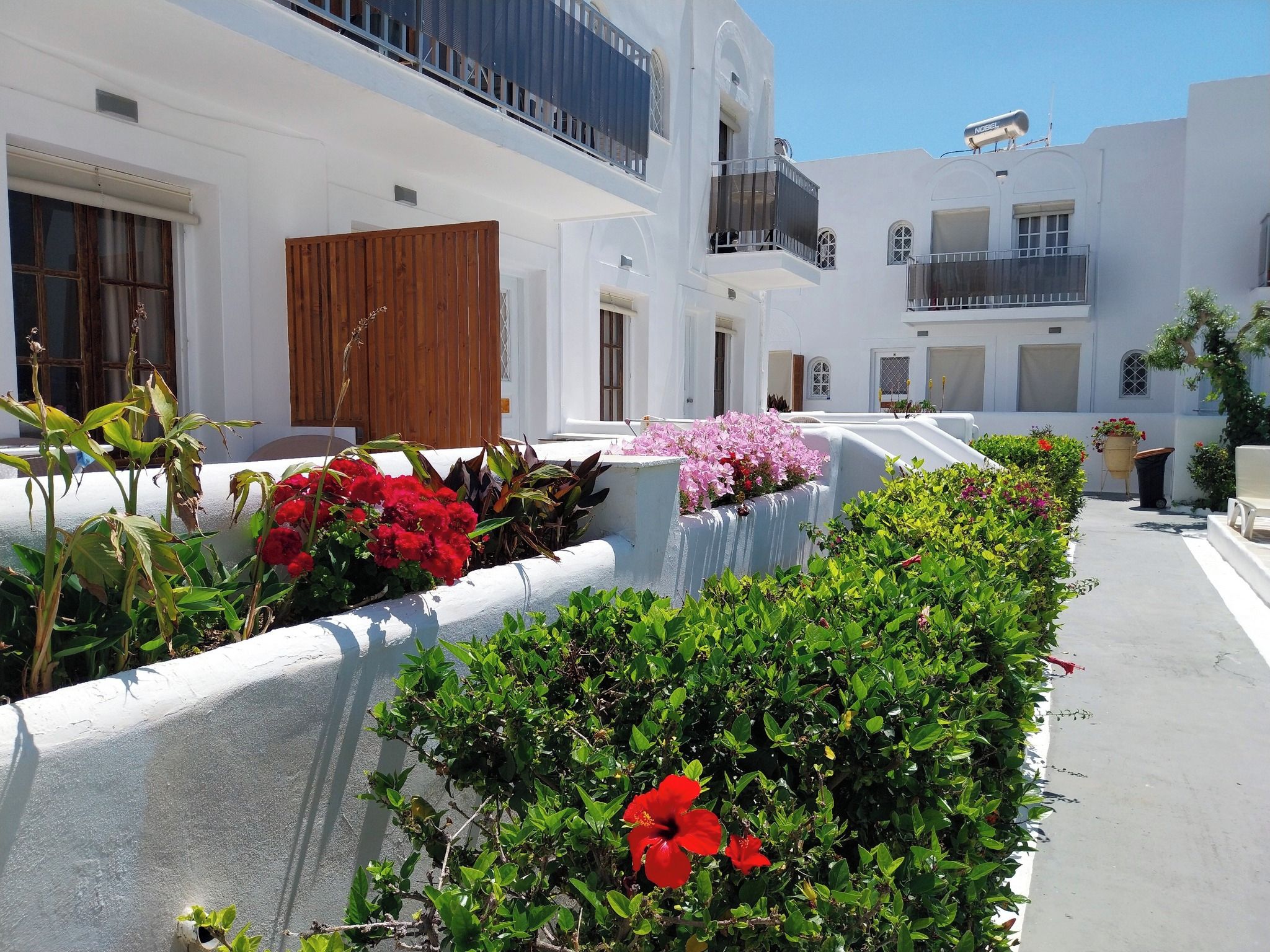 Un edificio blanco con balcones y un jardín con diversas plantas y flores.