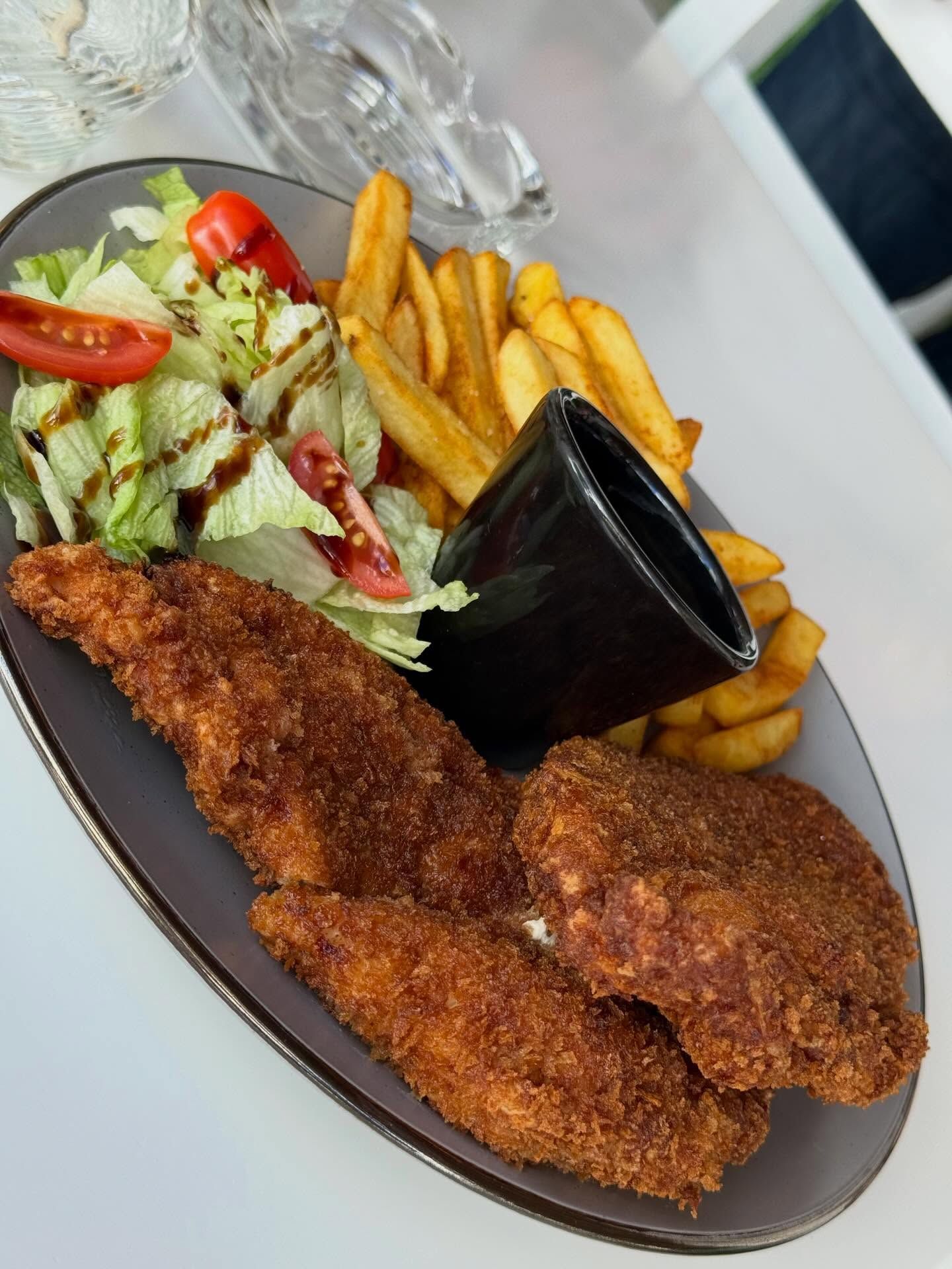 Ein Teller mit paniertem Schnitzel, Pommes und Salat mit dunkler Soße.