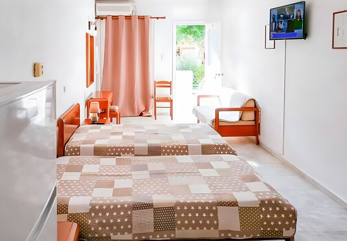 A bedroom with two beds, a TV, a desk, and a chair.