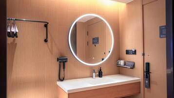 A modern bathroom with a round mirror, a sink, a hairdryer, and a towel rack.