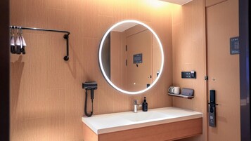 Un baño moderno con un espejo redondo, un lavabo, un secador de pelo y un perchero para toallas.