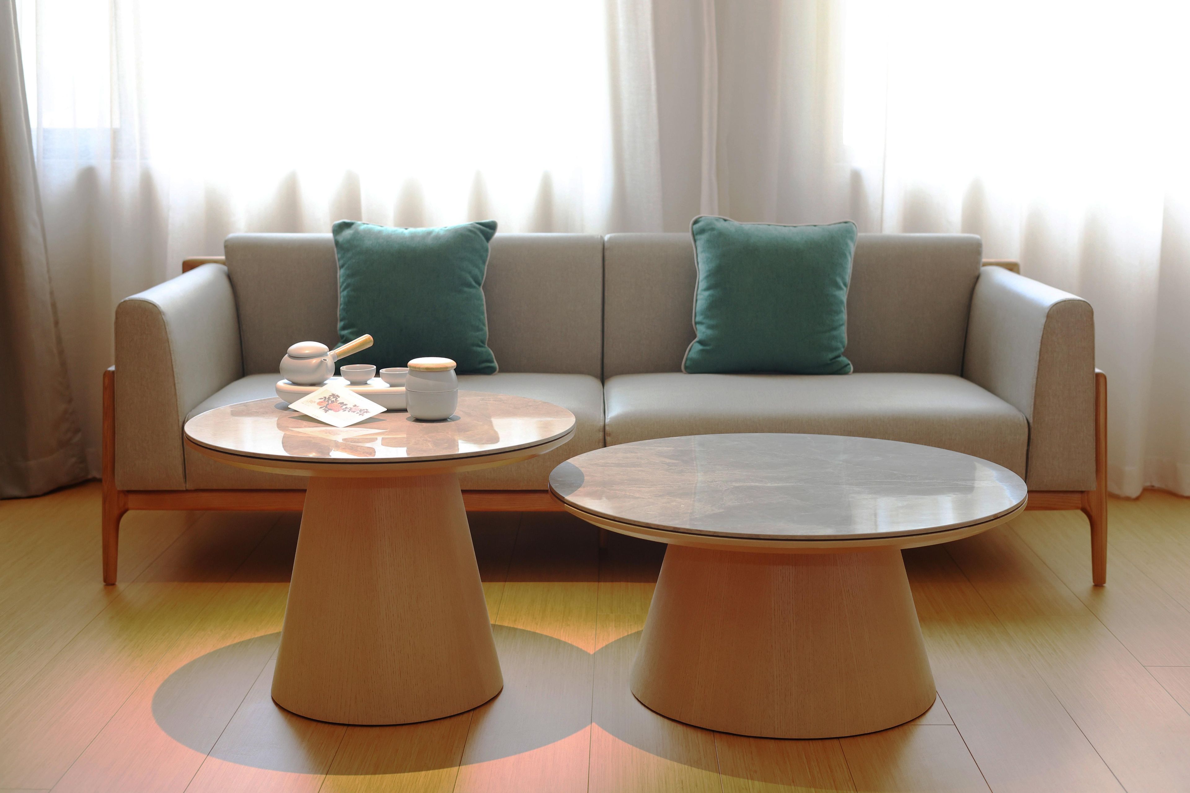 A modern living room with a sofa, two round wooden tables, and a set of tea utensils.