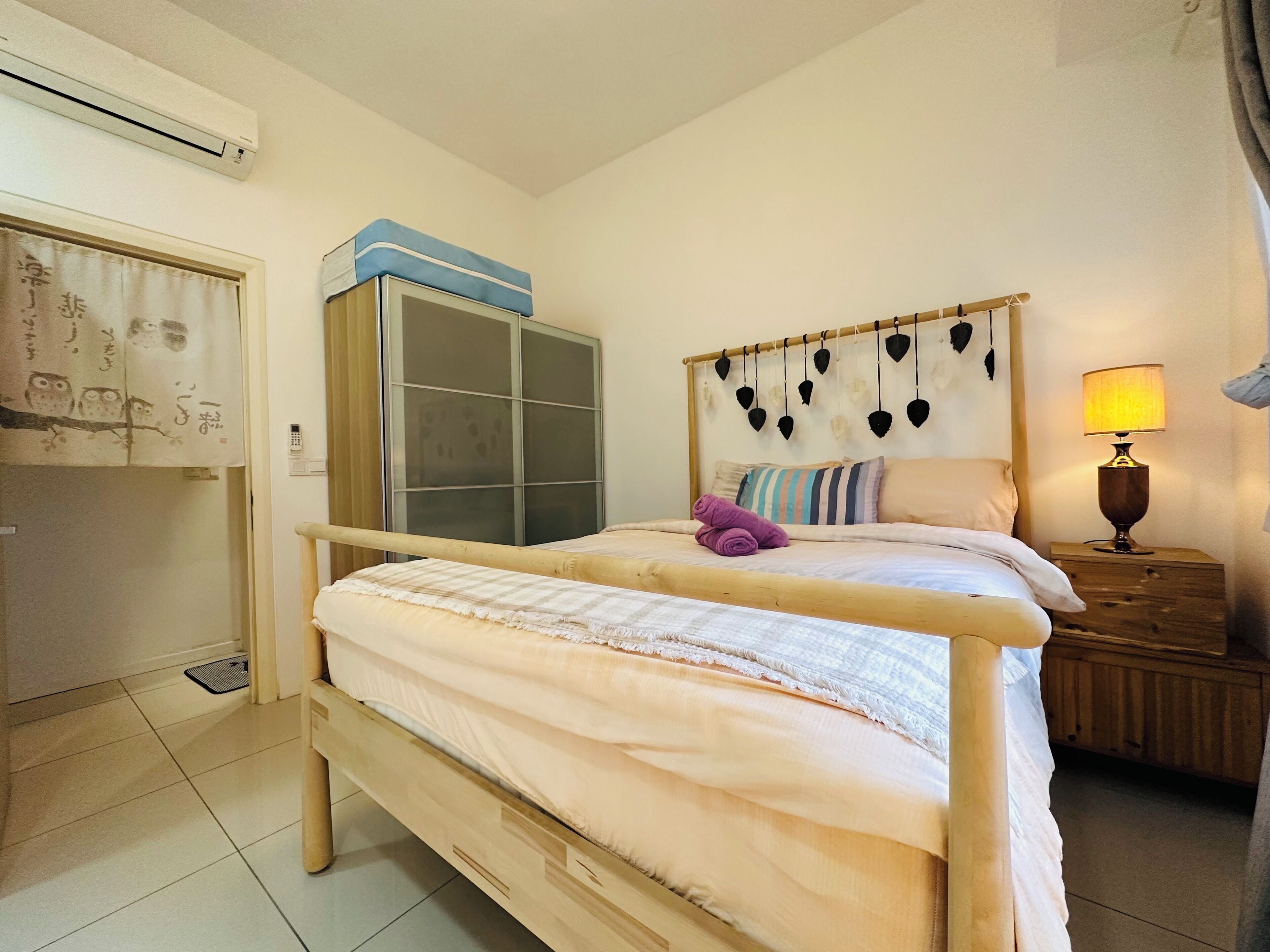 A bedroom with a wooden bed, a wardrobe, a bedside table with a lamp, and a wall-mounted heater.