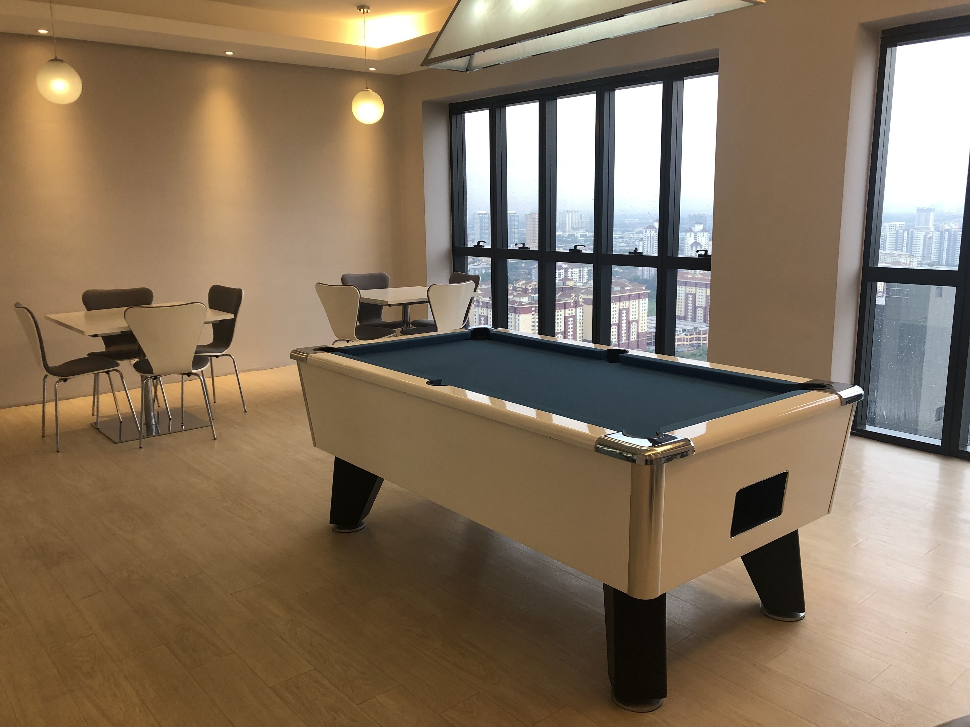 Mesa de billar en una habitación con vistas a la ciudad, una mesa y sillas, e iluminación colgante.